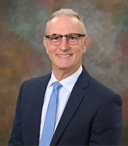 Mayor RIck Wash wears a dark blue jacket, light blue tie, and white shirt. He wears eyeglasses.